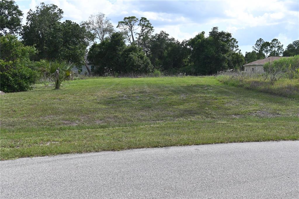 A vacant, grassy residential lot is situated between trees and neighboring houses — CHARMER LANE, NORTH PORT, FL