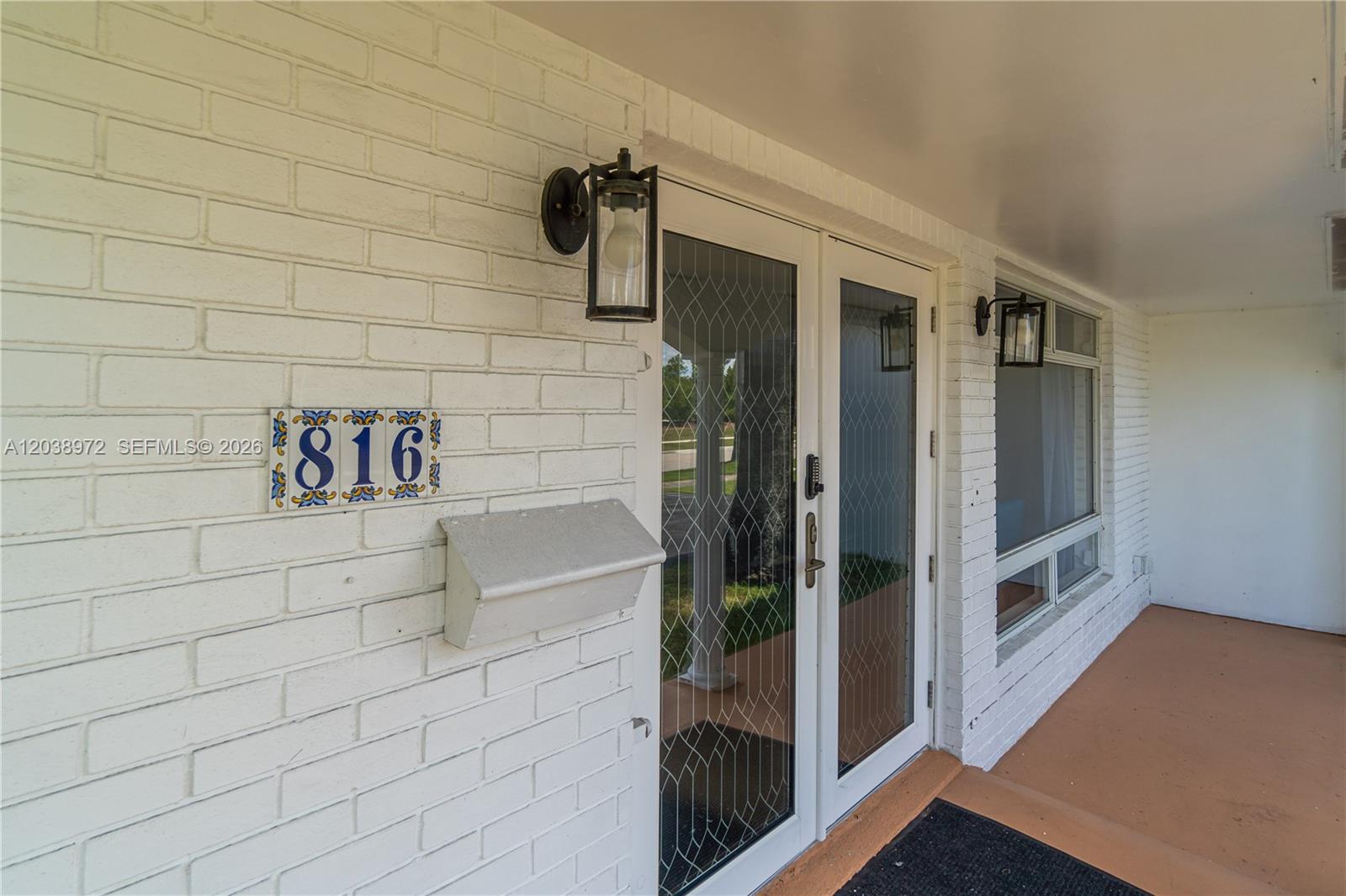 A white brick exterior wall features a house number plaque, mailbox, and double glass doors — 816 Polk St # 1, Hollywood FL 33019, HOLLYWOOD, FL