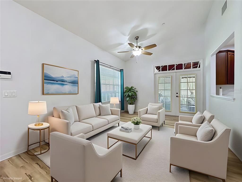 This living room features light-colored furniture, a ceiling fan, and glass doors leading outside — 102 CARRICK BEND WAY, CLERMONT, FL
