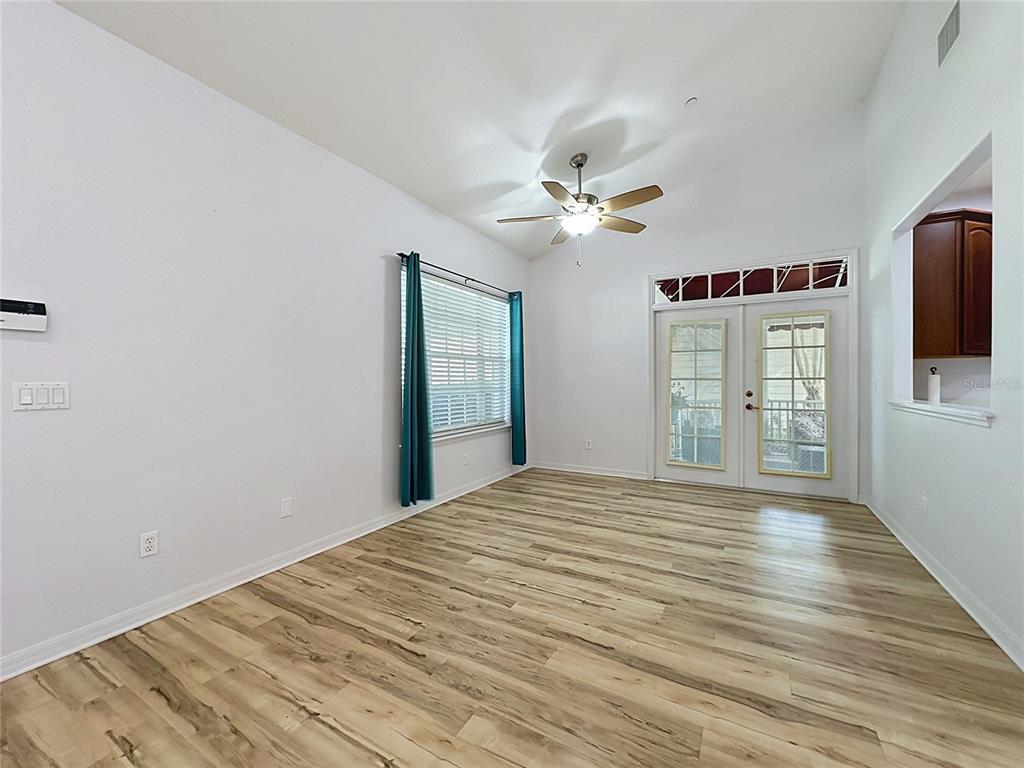 An empty room features light wood-look flooring, white walls, a ceiling fan, and glass-paned double doors — 102 CARRICK BEND WAY, CLERMONT, FL