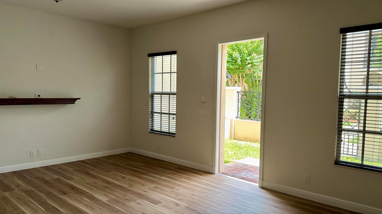 An empty room with wood-look flooring, a wall-mounted shelf, two windows, and a glass door — 814 NW 82nd Place, Boca Raton FL 33487, BOCA RATON, FL