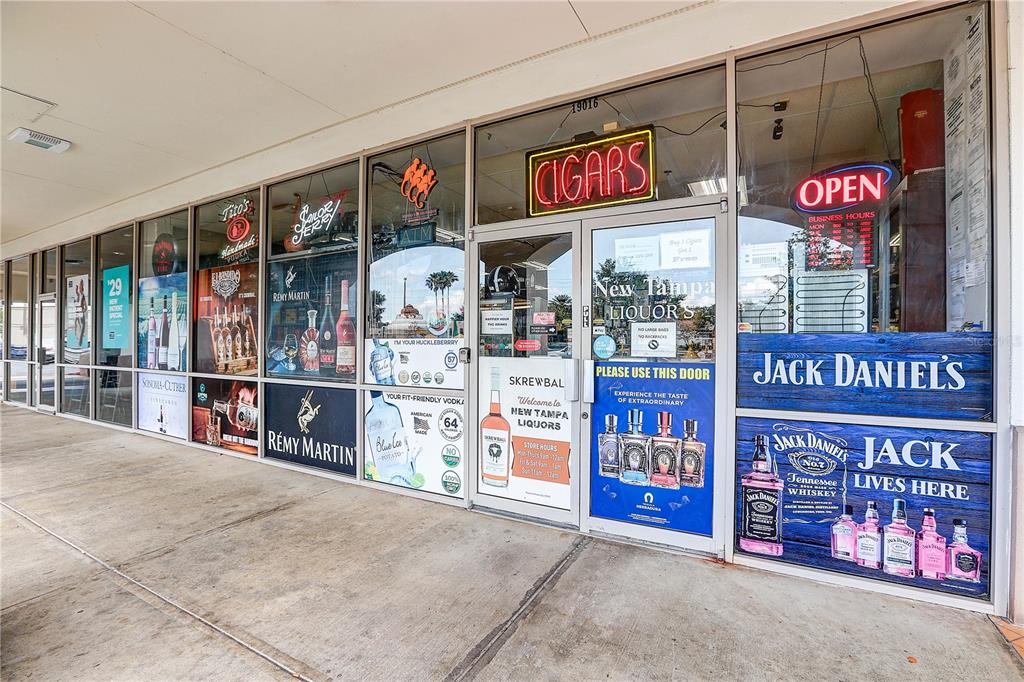 The exterior storefront of a liquor store features glass windows with various alcohol brand advertisements — BRUCE B DOWNS BOULEVARD, TAMPA, FL