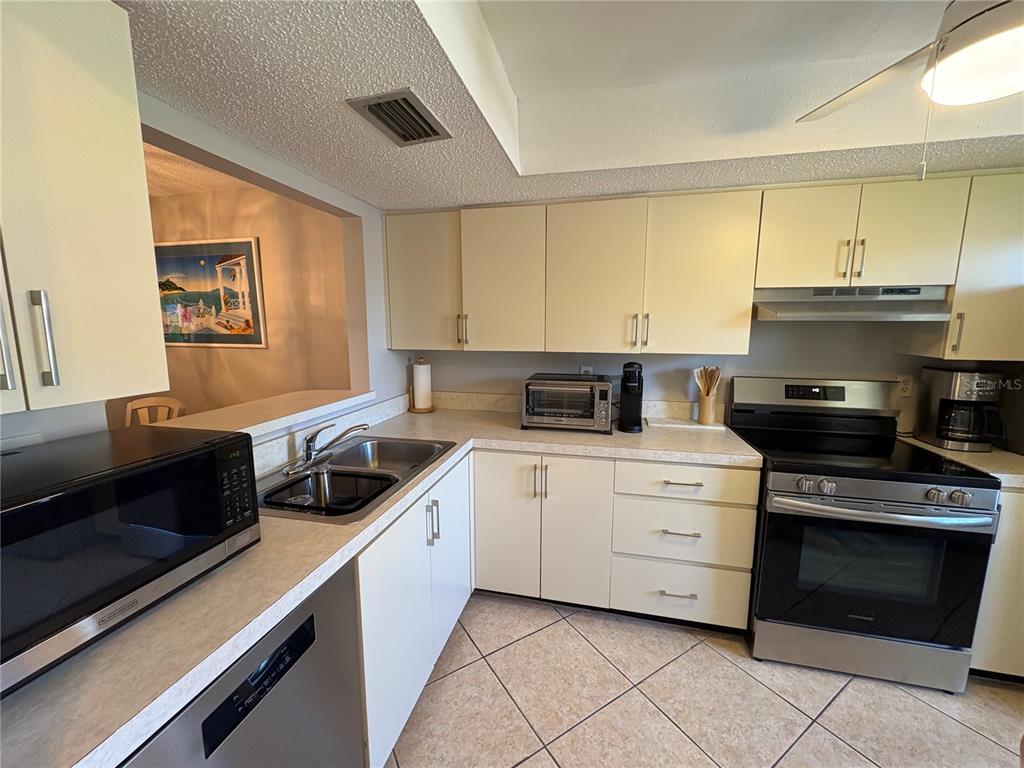 A kitchen features light-colored cabinets, stainless steel appliances, laminate countertops, and diagonal floor tiles — 2666 WOODGATE LANE UNIT D-1, SARASOTA, FL