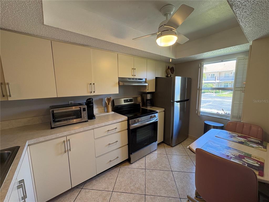 A kitchen features light-colored cabinets, stainless steel appliances, tile flooring, and a small dining area — 2666 WOODGATE LANE UNIT D-1, SARASOTA, FL