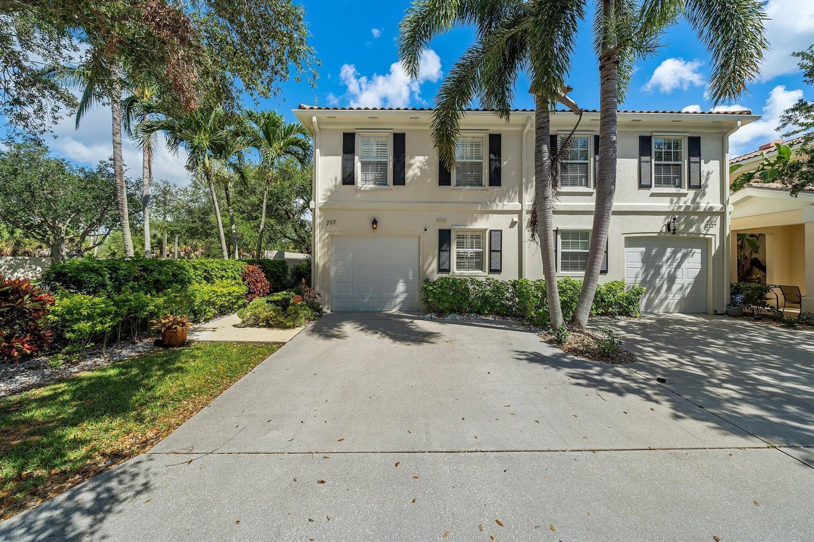 A two-story townhouse with a concrete driveway, a single-car garage, and palm trees — 2117 Tigris Drive, West Palm Beach FL 33411, WEST PALM BEACH, FL