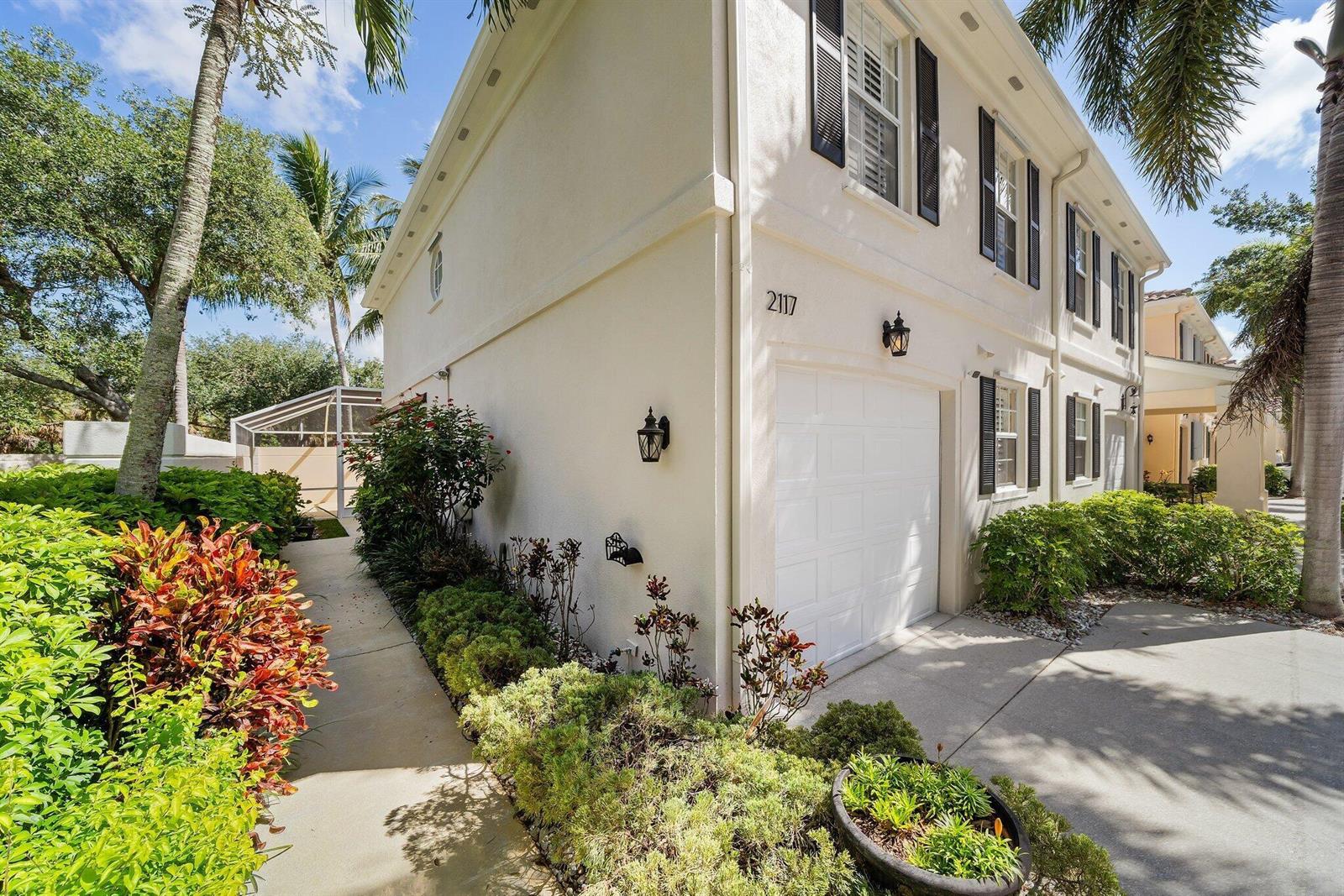 A two-story townhouse exterior with a white garage, black shutters, and a landscaped walkway — 2117 Tigris Drive, West Palm Beach FL 33411, WEST PALM BEACH, FL