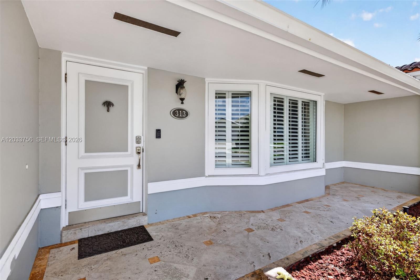 The exterior entrance features a white door, a bay window, and stone tile flooring — 313 SE 6th St, Dania Beach FL 33004, DANIA BEACH, FL