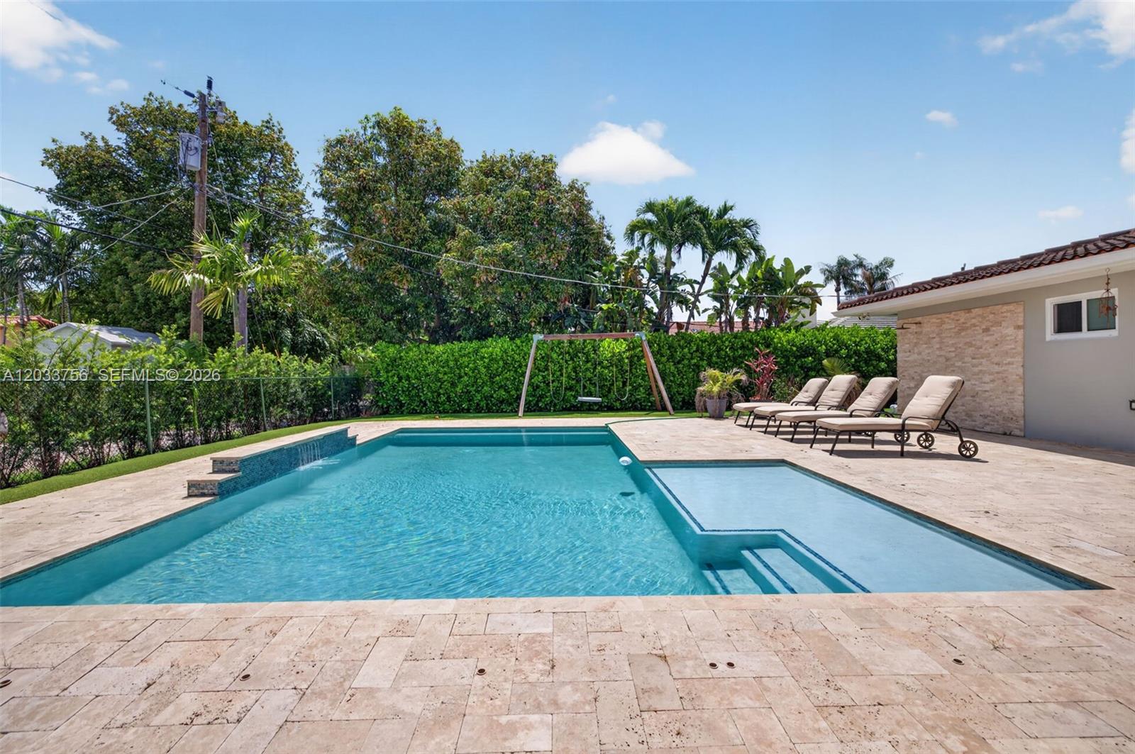 A rectangular swimming pool with a sun shelf sits on a stone patio with lounge chairs — 313 SE 6th St, Dania Beach FL 33004, DANIA BEACH, FL
