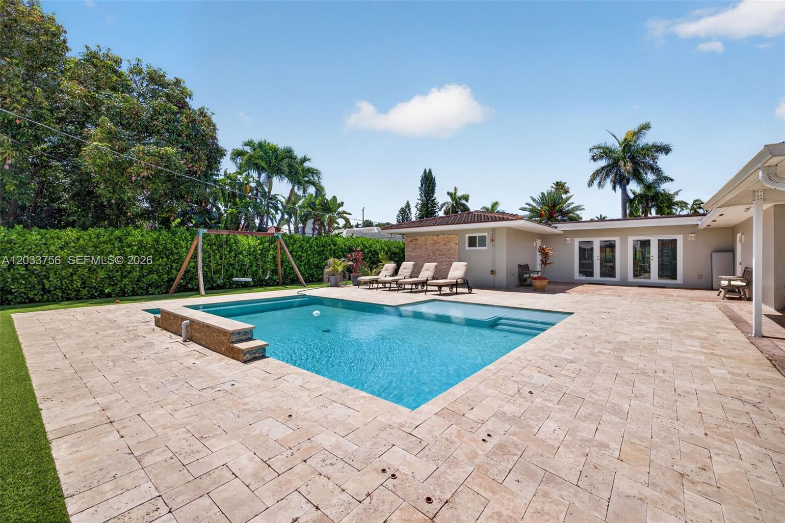 A rectangular swimming pool sits on a stone patio next to a house and lawn — 313 SE 6th St, Dania Beach FL 33004, DANIA BEACH, FL