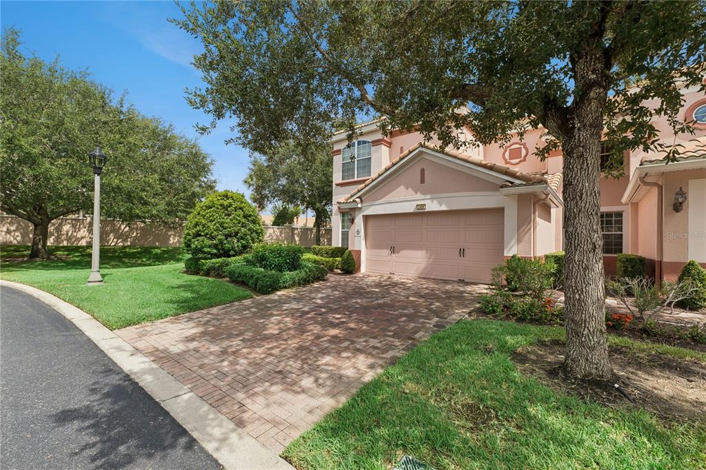 A two-story house with a beige stucco exterior, a brick paver driveway, and a two-car garage — 1406 MILLEDGE LANE, DAVENPORT, FL