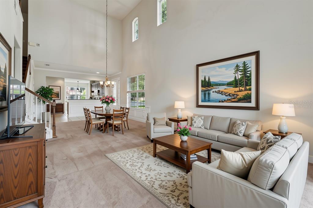 A high-ceilinged living and dining area features neutral furniture, a large landscape painting, and carpeting — 1406 MILLEDGE LANE, DAVENPORT, FL