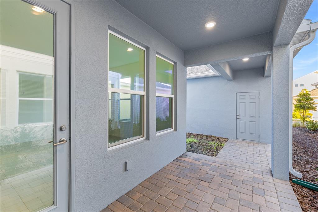A covered patio with light blue stucco walls, a paver floor, and two large windows — 15154 ALDER CHASE ALLEY, WINTER GARDEN, FL