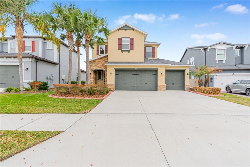 A two-story suburban house with a three-car garage, tan stucco siding, and palm trees — 3963 EMPOLI COURT, WESLEY CHAPEL, FL