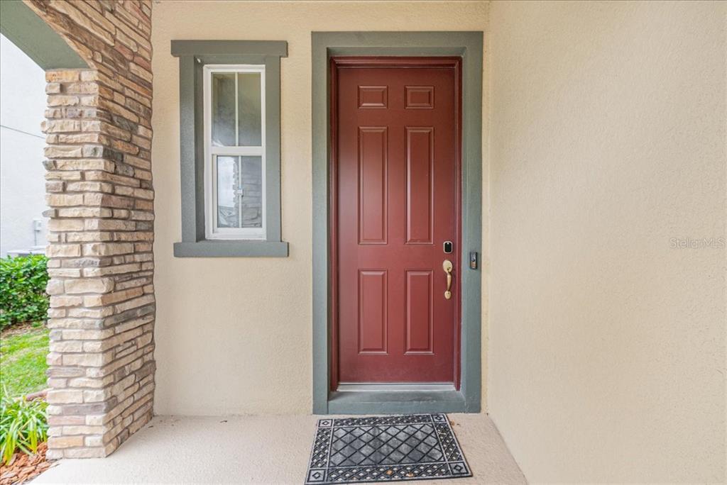 A red front door with a window and stone siding sits on a covered porch — 3963 EMPOLI COURT, WESLEY CHAPEL, FL