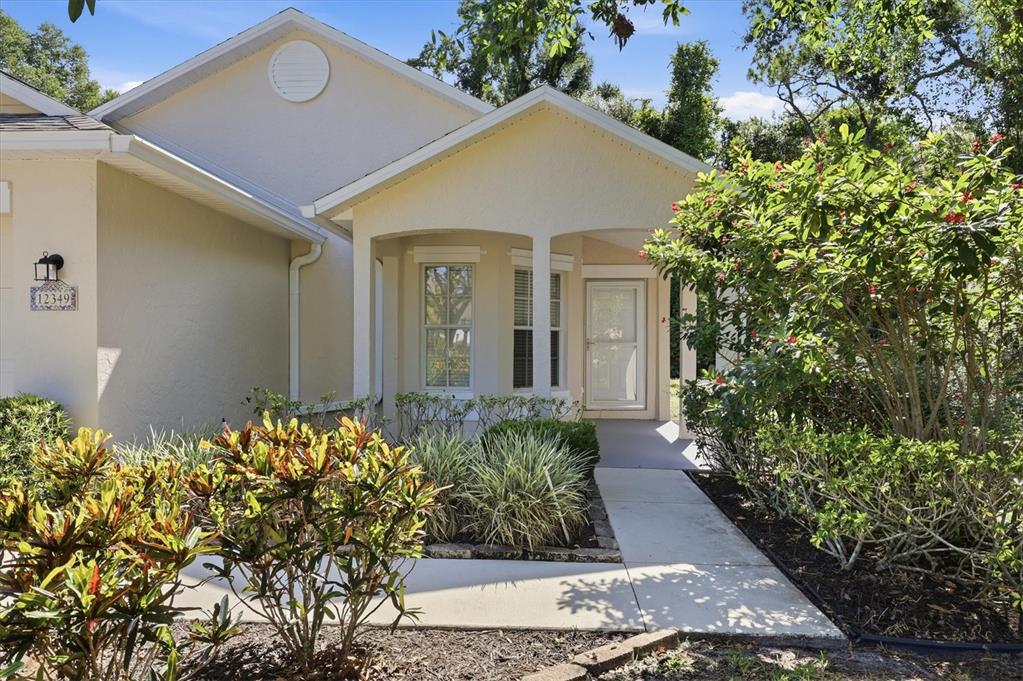 A beige house exterior features a covered entryway, a concrete walkway, and landscaped front gardens — 12349 WOOD SAGE TERRACE, BRADENTON, FL