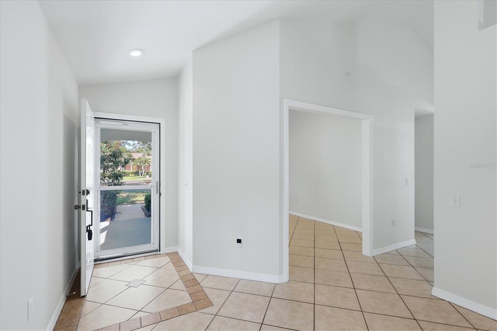An entryway with light-colored tile flooring leads to an open interior space and front door — 12349 WOOD SAGE TERRACE, BRADENTON, FL