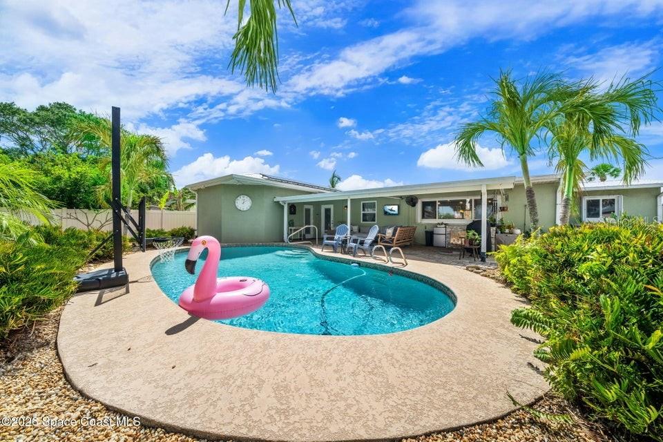 A backyard features a swimming pool with a pink flamingo float and a covered patio — 121 ALGONQUIN TERRACE, INDIAN HARBOUR BEACH, FL