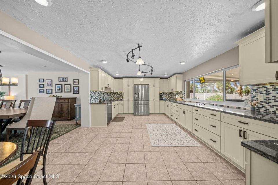 A spacious kitchen features light-colored cabinetry, granite countertops, tile flooring, and a large window — 121 ALGONQUIN TERRACE, INDIAN HARBOUR BEACH, FL