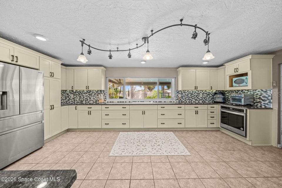 A kitchen features cream-colored cabinets, stainless steel appliances, a tile backsplash, and track lighting — 121 ALGONQUIN TERRACE, INDIAN HARBOUR BEACH, FL