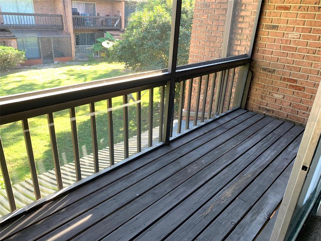 A screened-in balcony features dark wood decking, a brick wall, and a view of grass — 5123 PICADILLY CIRCUS COURT UNIT 2, ORLANDO, FL