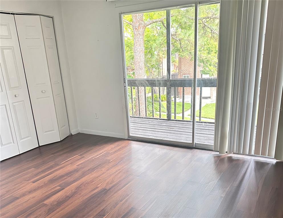 An empty room with wood-look flooring, a white closet, and a sliding glass door to a balcony — 5123 PICADILLY CIRCUS COURT UNIT 2, ORLANDO, FL