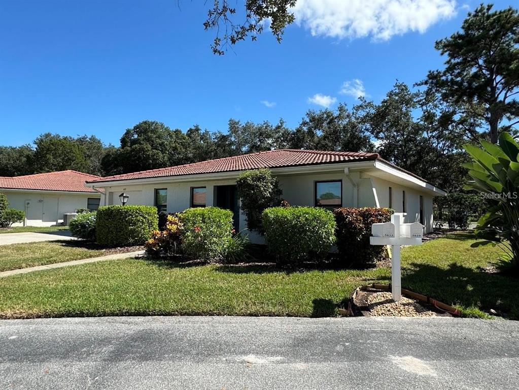 A single-story house with a tiled roof and manicured hedges sits behind a mailbox post — 5033 VIVIENDA WAY UNIT 19, SARASOTA, FL