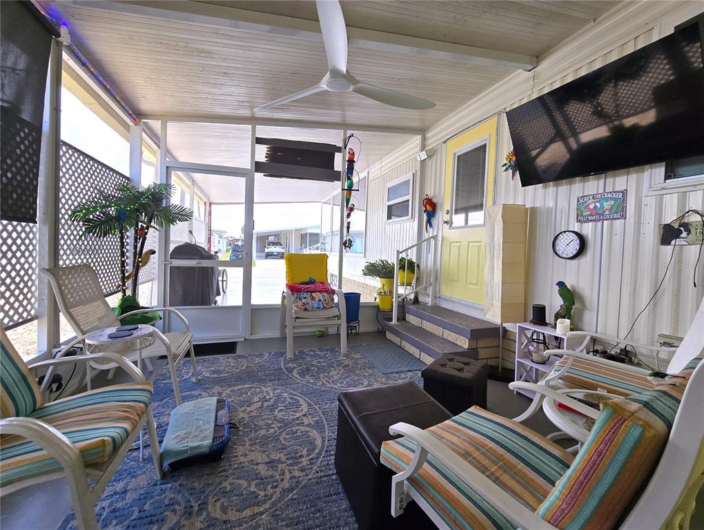 A screened-in porch features a blue patterned rug, patio furniture, and a wall-mounted television — 5619 BAYSHORE ROAD UNIT 435, PALMETTO, FL