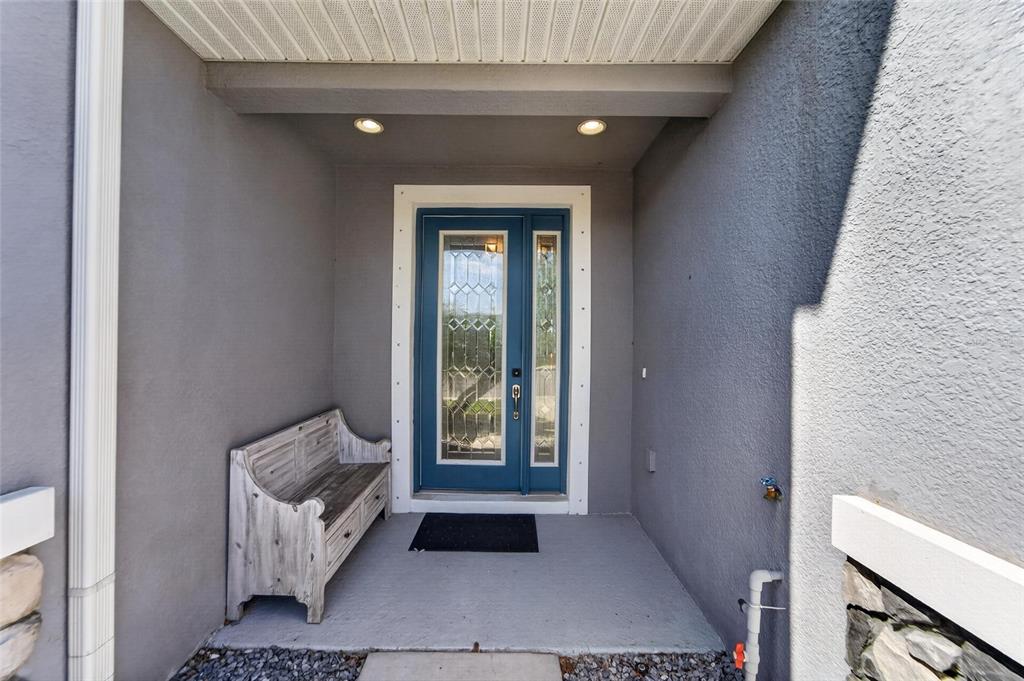 A covered entryway features a blue front door with glass panels and a wooden bench — 8108 MUDDY PINES PLACE, TAMPA, FL
