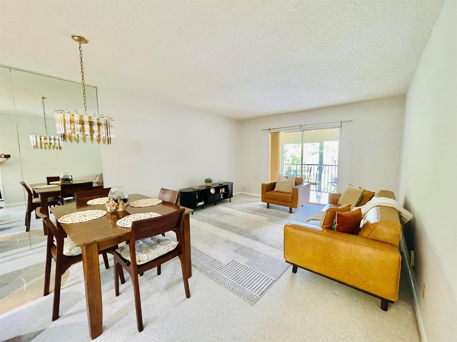 A living and dining area features a wooden table, leather sofa, and a glass chandelier — 257 S Cypress Road # 443, Pompano Beach FL 33060, POMPANO BEACH, FL