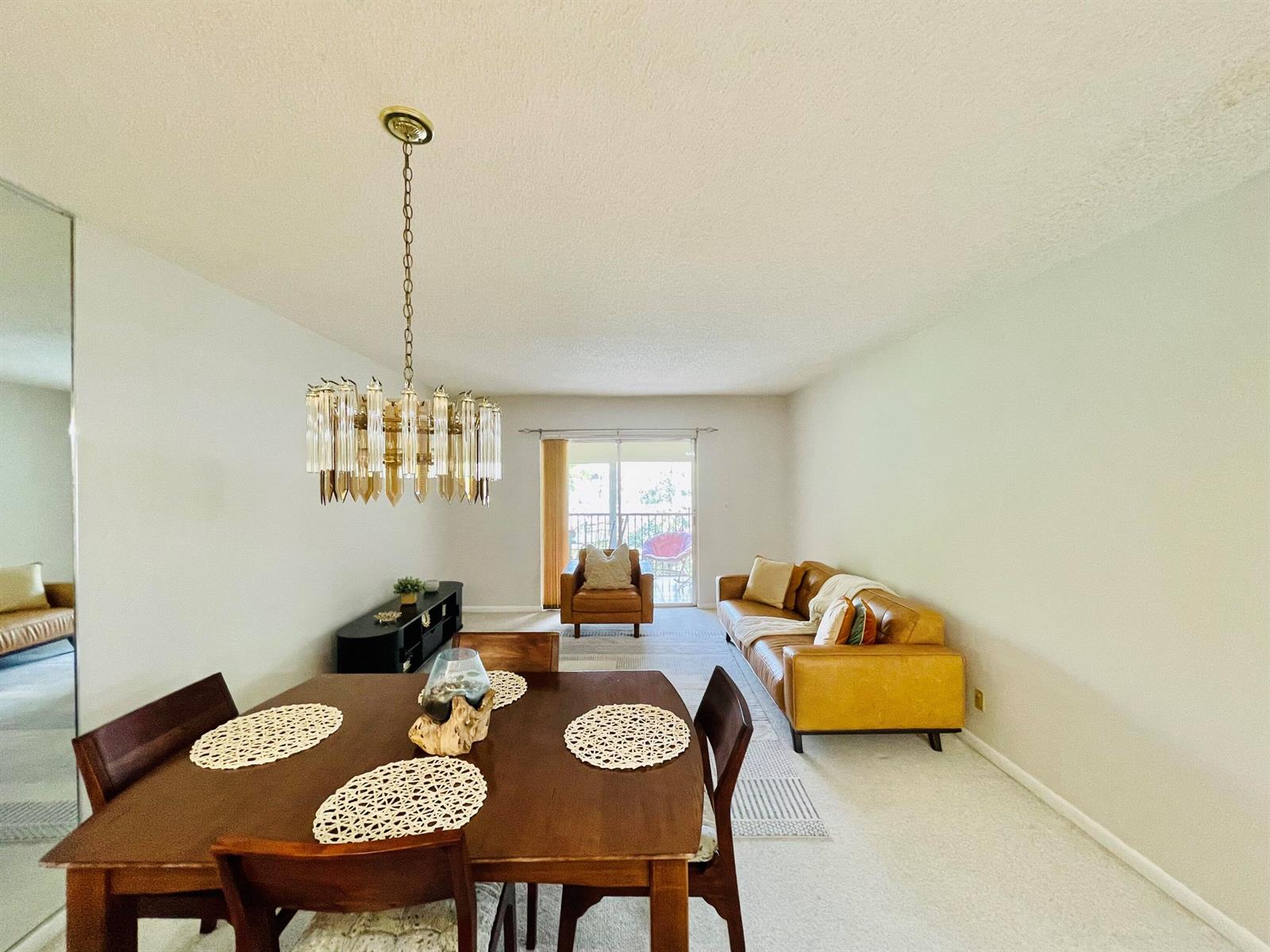 A dining area with a chandelier opens into a living room featuring a leather sofa — 257 S Cypress Road # 443, Pompano Beach FL 33060, POMPANO BEACH, FL