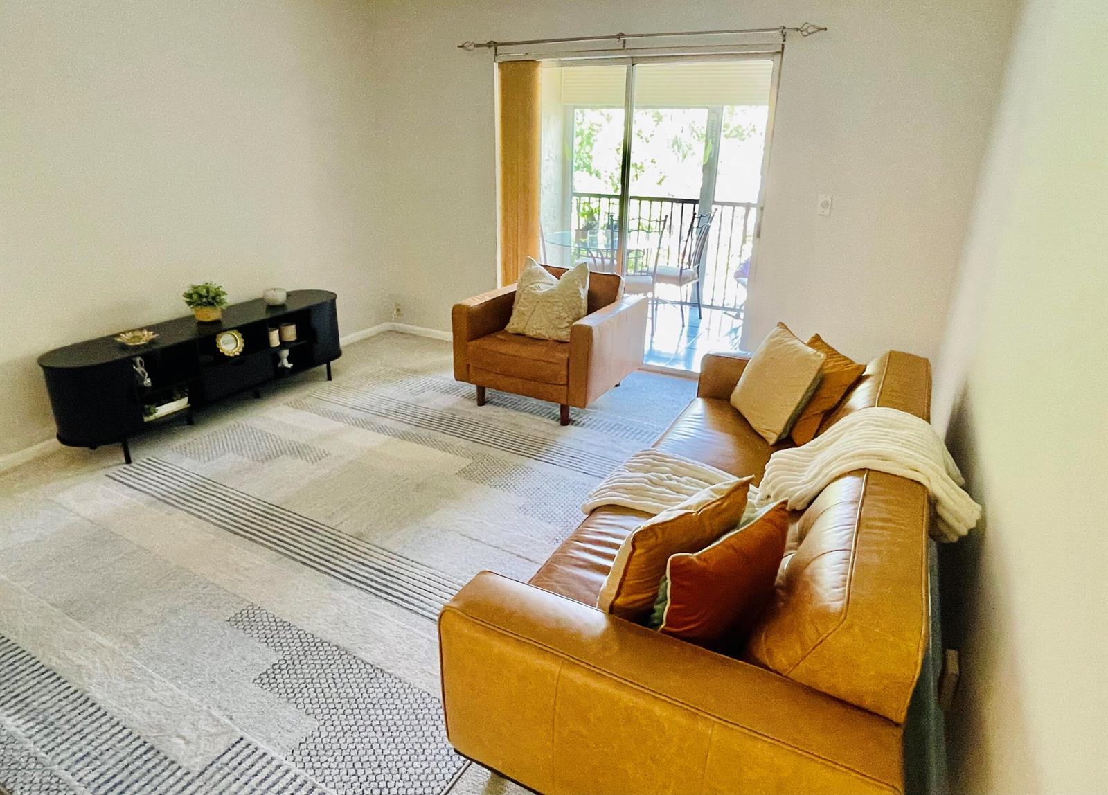 A living room features a leather sofa, matching armchair, black media console, and patterned rug — 257 S Cypress Road # 443, Pompano Beach FL 33060, POMPANO BEACH, FL