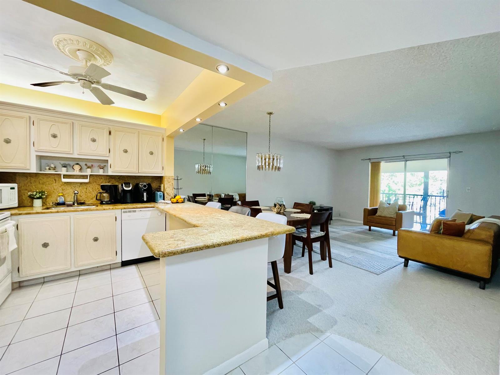 An open-concept kitchen with granite countertops overlooks a dining area and living room — 257 S Cypress Road # 443, Pompano Beach FL 33060, POMPANO BEACH, FL