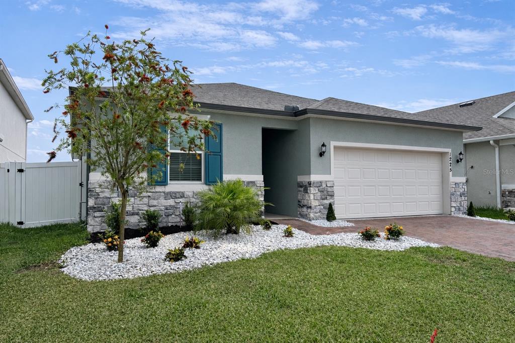 A single-story house with a light green exterior, stone veneer, and a two-car garage — 1225 FOX HEDGE LANE, ST CLOUD, FL