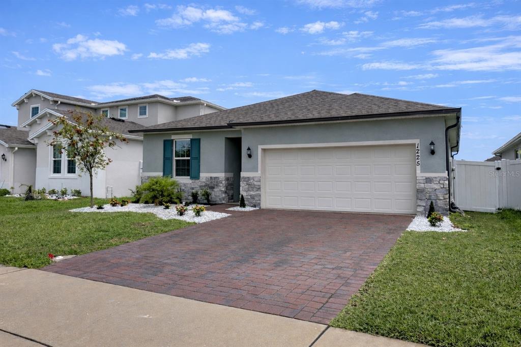 A single-story house with a gray stucco exterior, stone accents, and a paved driveway — 1225 FOX HEDGE LANE, ST CLOUD, FL