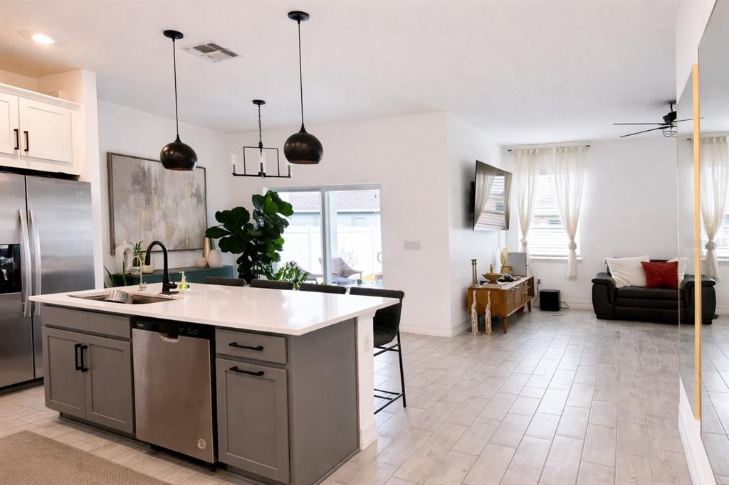A modern kitchen with a gray island and stainless steel appliances opens to a living area — 1225 FOX HEDGE LANE, ST CLOUD, FL