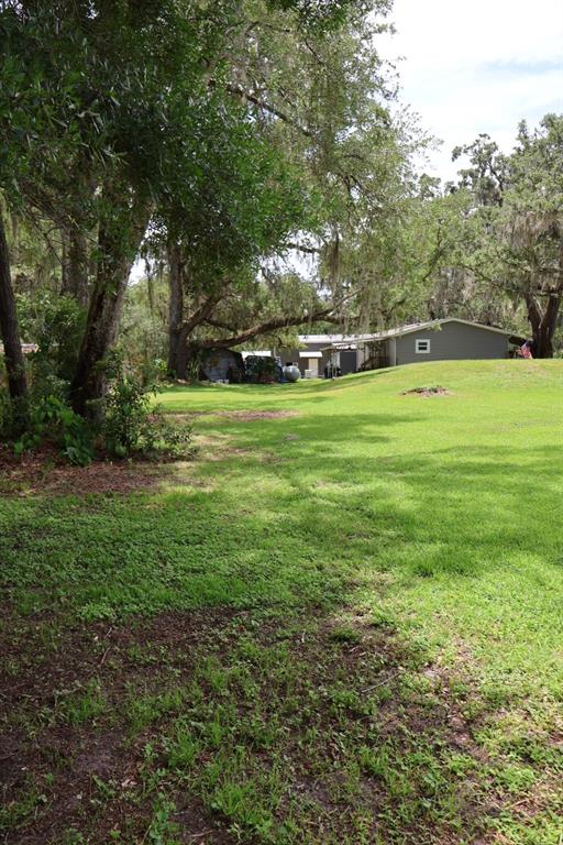 A grassy yard leads toward a gray house shaded by large, moss-covered oak trees — 9028 WEST STREET, BROOKSVILLE, FL