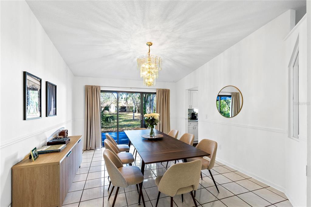 A dining room features a long wooden table, six chairs, a chandelier, and sliding glass doors — 710 BRIARWOOD DRIVE, WINTER SPRINGS, FL