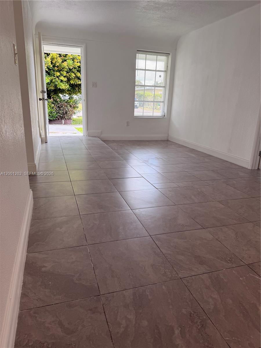 An empty room features light-colored tile flooring, white walls, a window, and an open door — 6613 Evergreen Dr # A, Miramar FL 33023, MIRAMAR, FL
