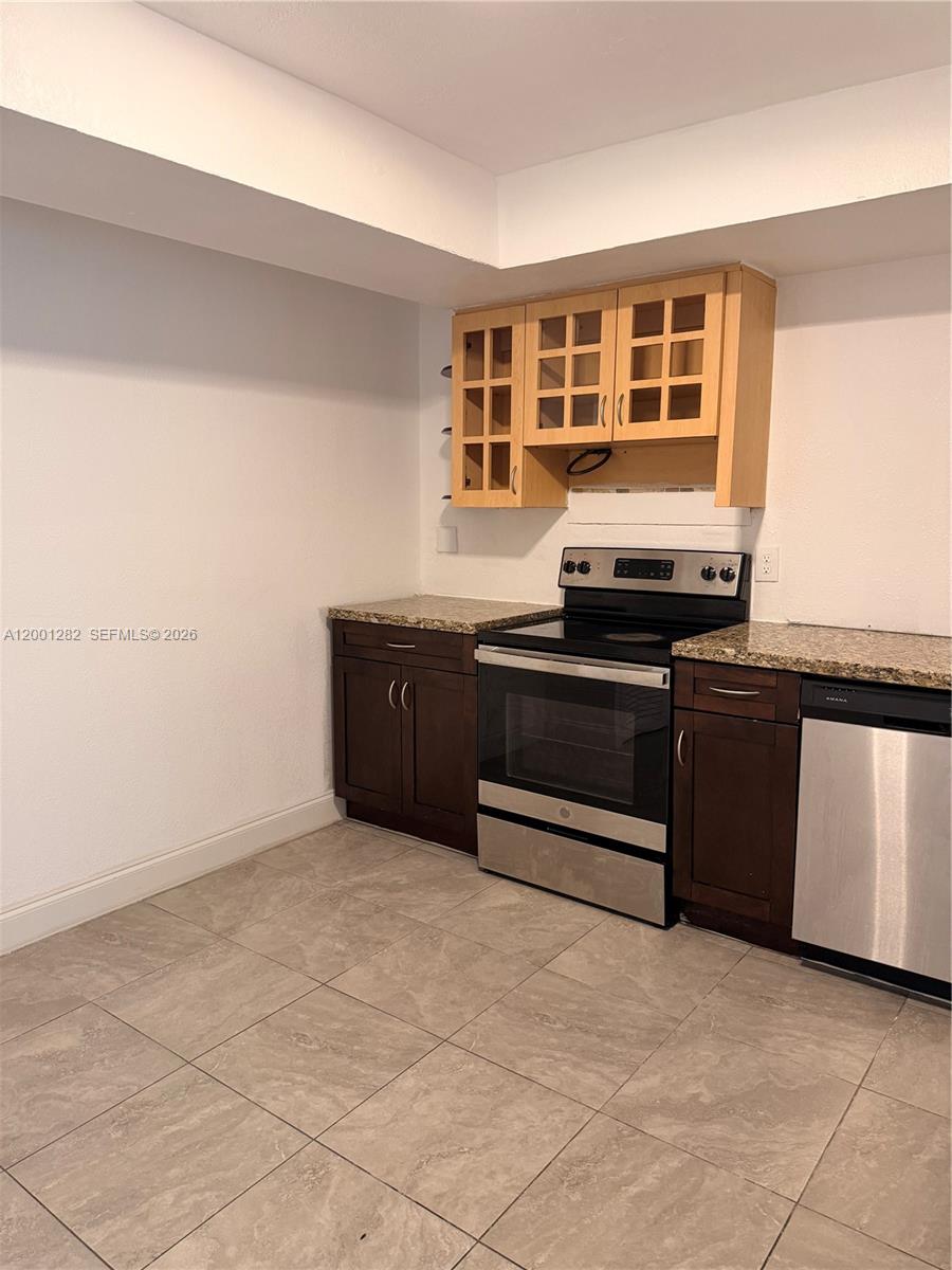 A kitchen features dark wood cabinets, granite countertops, stainless steel appliances, and light tile flooring — 6613 Evergreen Dr # A, Miramar FL 33023, MIRAMAR, FL