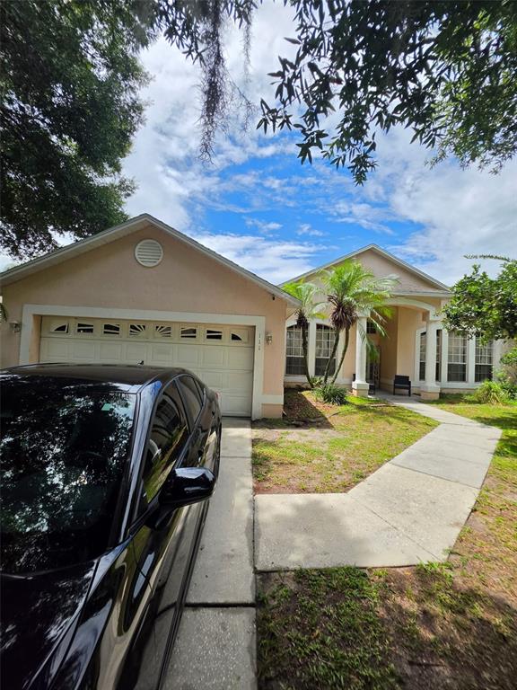 A single-story house with a beige exterior, a two-car garage, and a concrete walkway — 111 SUNRIDGE WOODS COURT, DAVENPORT, FL