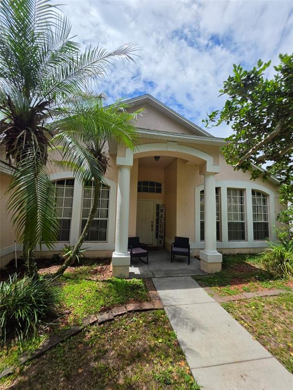 The exterior of a single-story house features a covered entryway with columns and a walkway — 111 SUNRIDGE WOODS COURT, DAVENPORT, FL