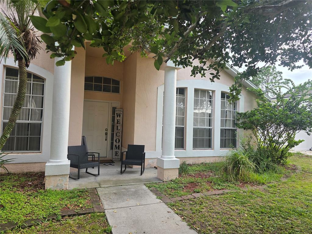 The exterior of a peach-colored house features a covered entryway with two white columns — 111 SUNRIDGE WOODS COURT, DAVENPORT, FL