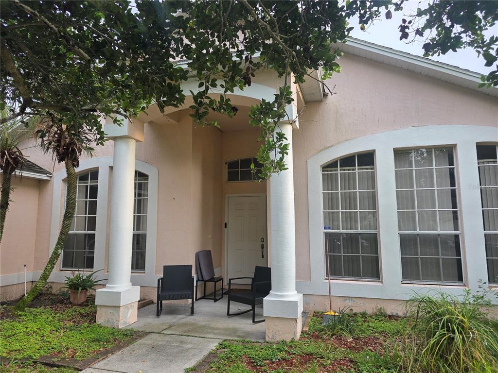 A pink stucco house exterior features a covered entryway with two white columns and chairs — 111 SUNRIDGE WOODS COURT, DAVENPORT, FL