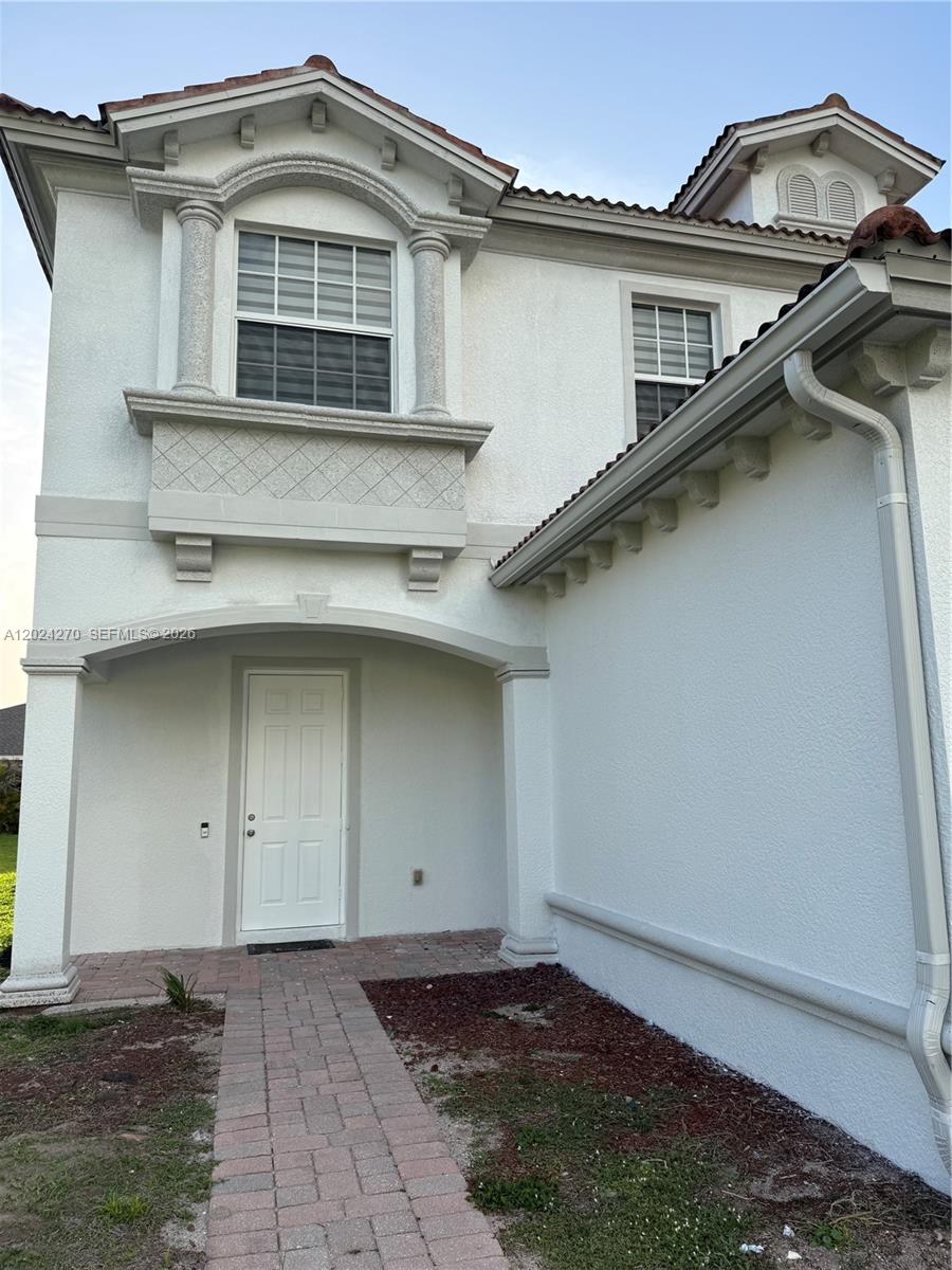 The exterior of a two-story house features a white stucco facade, arched entryway, and tiled roof — 9135 Leatherwood Loop, Lehigh Acres FL 33936, LEHIGH ACRES, FL
