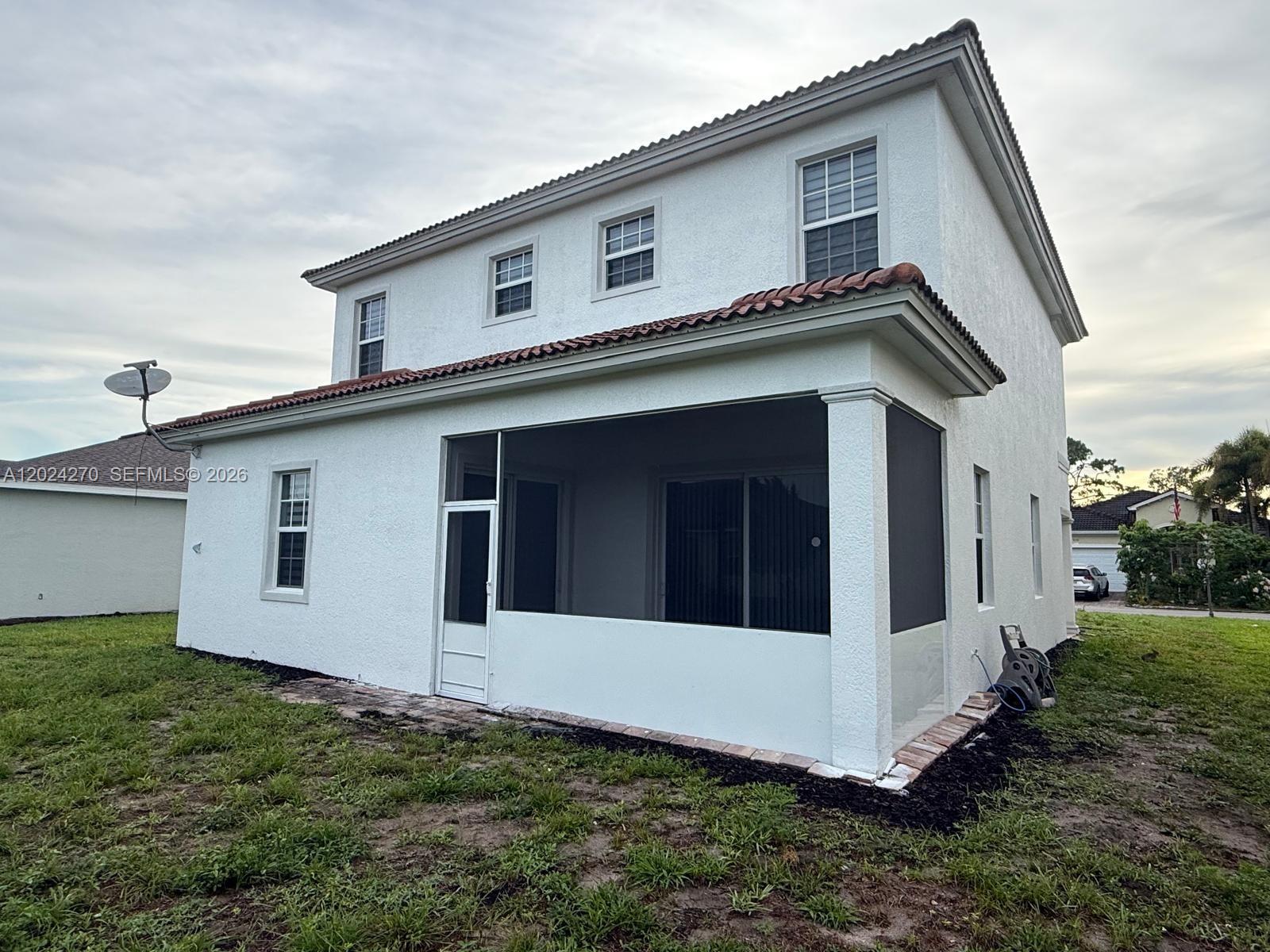 The exterior of a two-story white stucco house features a screened-in patio and tile roof — 9135 Leatherwood Loop, Lehigh Acres FL 33936, LEHIGH ACRES, FL