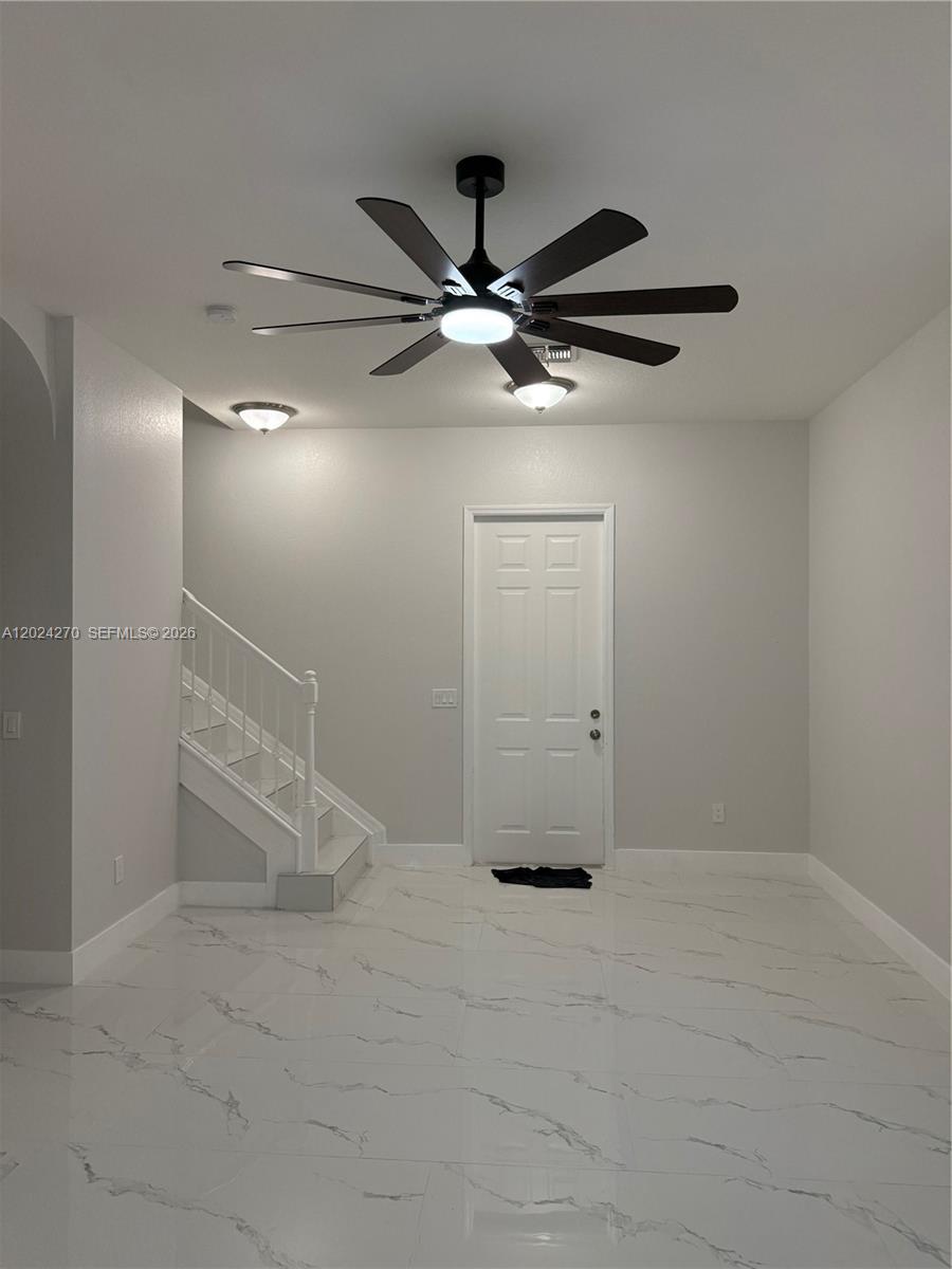 A room with white marble-look tile flooring, a ceiling fan, and a staircase — 9135 Leatherwood Loop, Lehigh Acres FL 33936, LEHIGH ACRES, FL