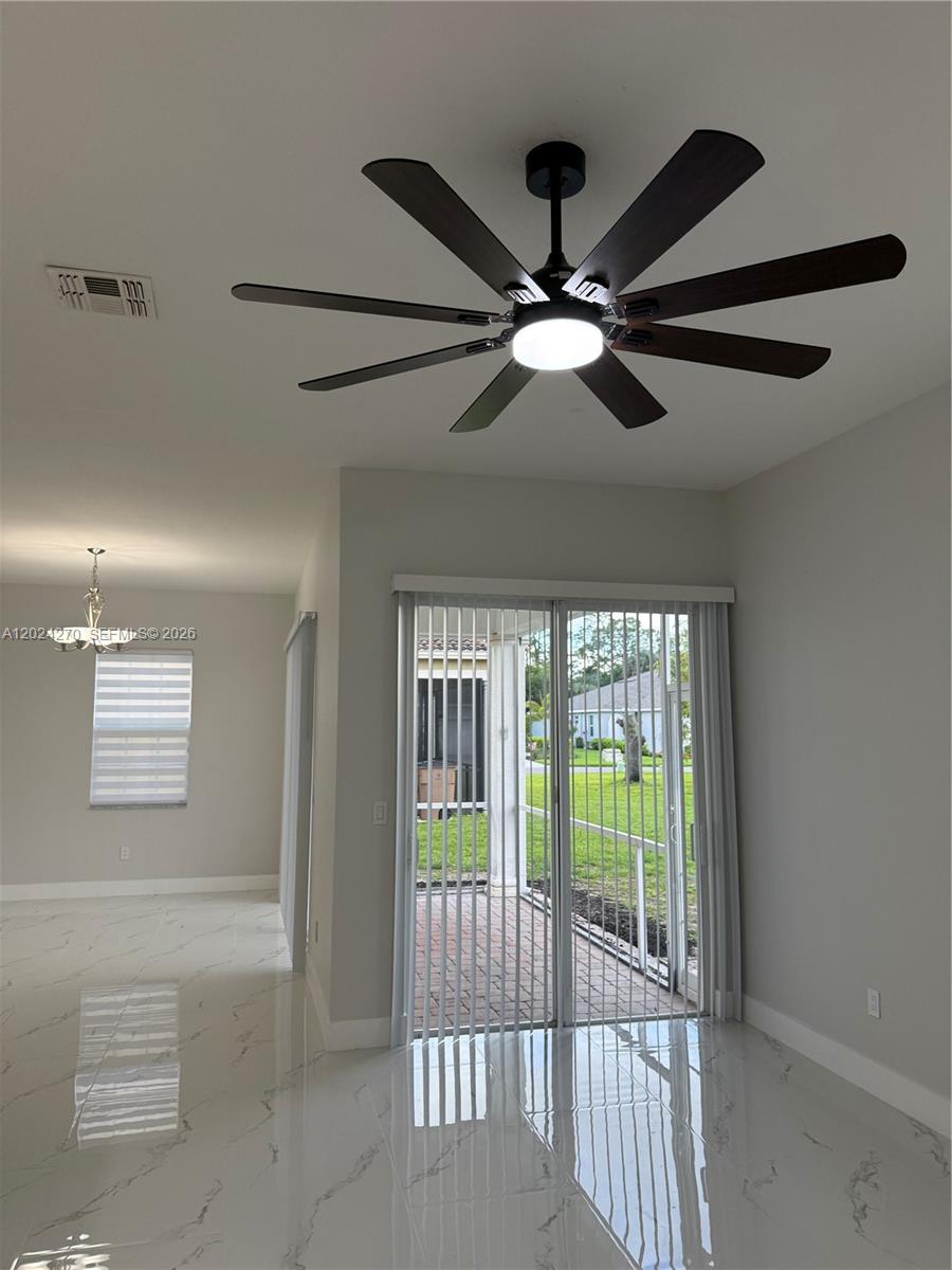 A room with white marble-look tile floors, a ceiling fan, and sliding glass patio doors — 9135 Leatherwood Loop, Lehigh Acres FL 33936, LEHIGH ACRES, FL