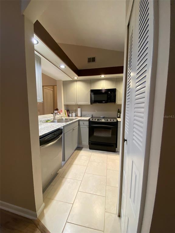 A kitchen features light-colored cabinets, granite countertops, black appliances, and light tile flooring — 3118 S SEMORAN BOULEVARD UNIT N8, ORLANDO, FL