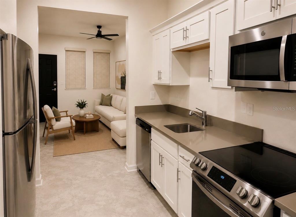 A kitchen with white cabinets and stainless steel appliances opens into a living room area — 8979 CHIPPING SQUARE LANE, DAVENPORT, FL