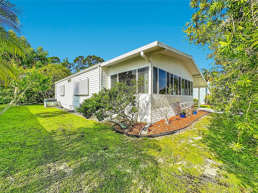 A white mobile home with a screened-in porch sits on a grassy lot with trees — 8227 CINNAMON LANE, PORT ST LUCIE, FL